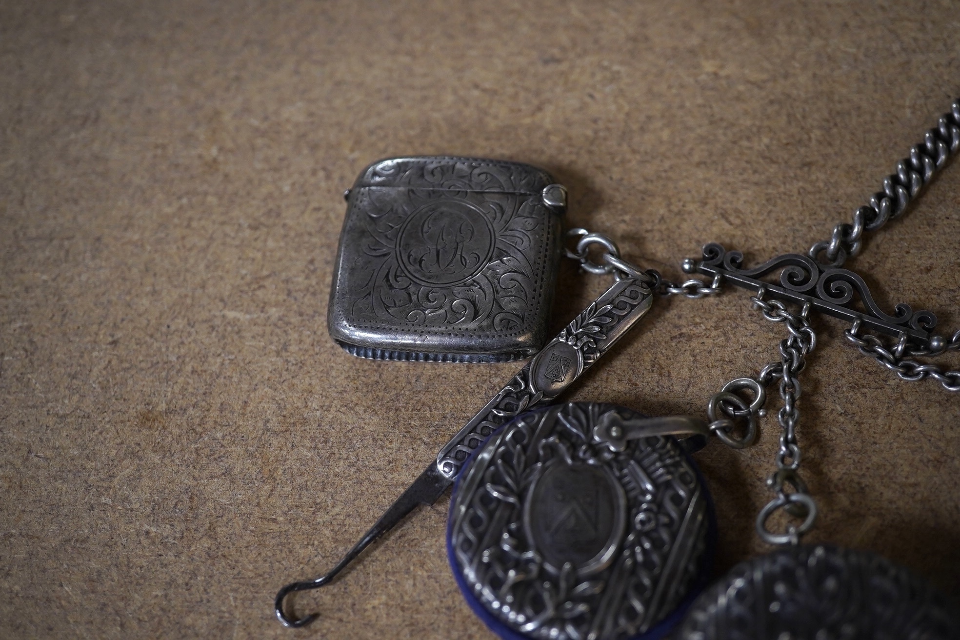 An early 20th century French white metal chatelaine, hung with six accoutrements including an associated silver vesta case, overall 35cm. Condition - fair